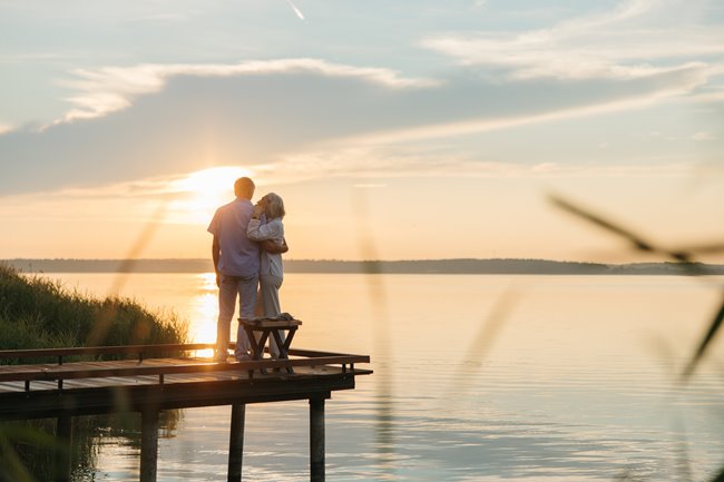 Stel met ondergaande zon op aanlegsteiger bij meer